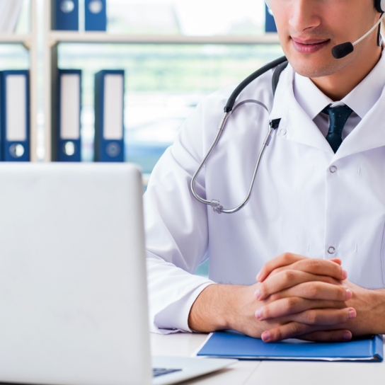 a doctor sits in front of a laptop, conducting a telehealth appointment