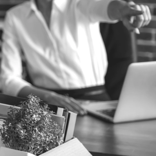 a boss pointing toward an exit while an employee carries a box of belongings